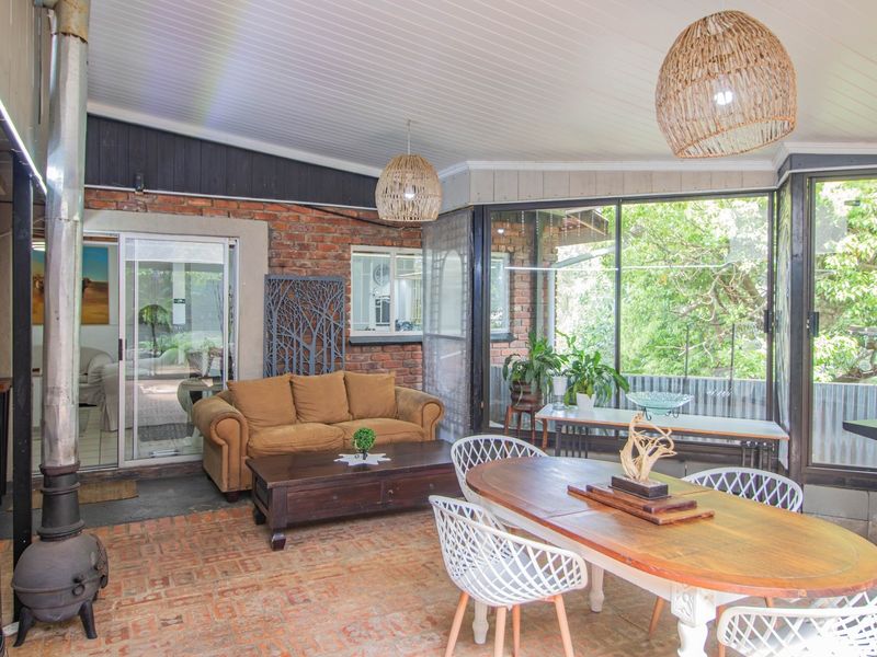 Spacious covered patio featuring exposed brick walls, a wood-burning stove, and large glass windows overlooking the garden.