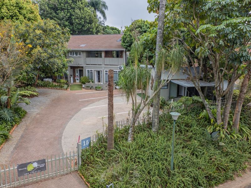 A well-maintained two-story property featuring a paved driveway, established garden, and a balcony, presenting a welcoming front facade.