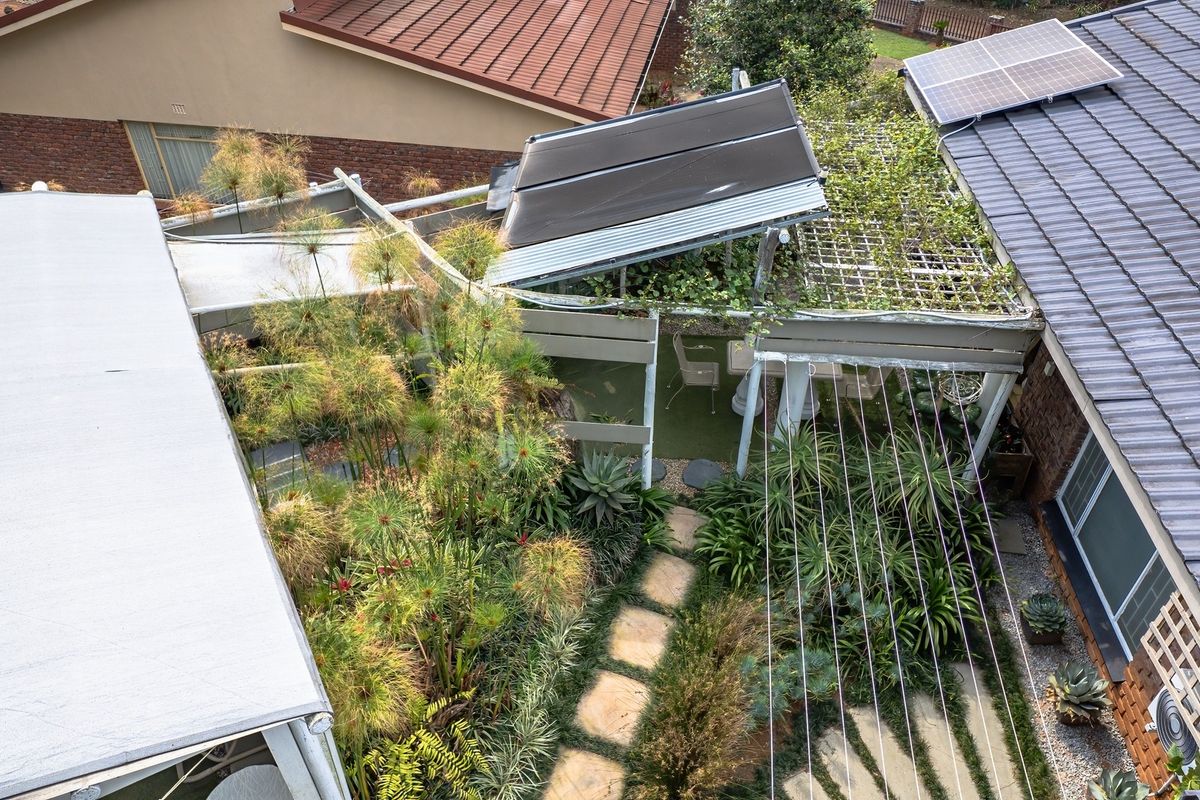 Aerial view of the property showing the roof structure, solar installations, and a landscaped garden area with a pergola and paved pathways.