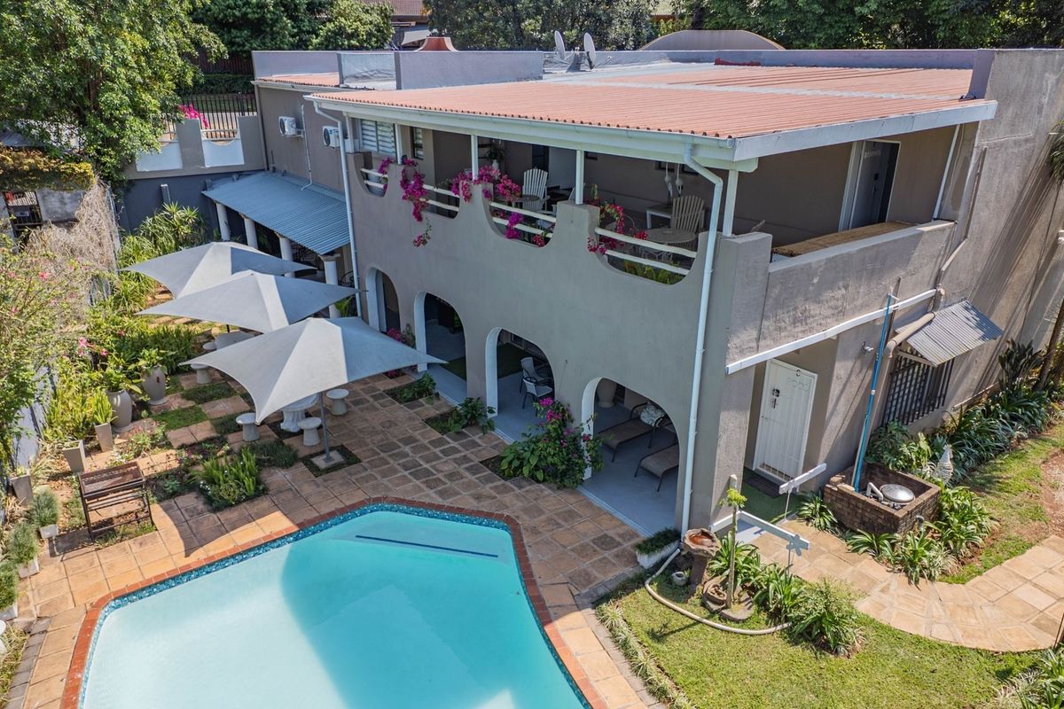 Aerial view of the rear exterior featuring a swimming pool, paved patio area, and a two-story structure with a balcony and covered ground-floor patio.