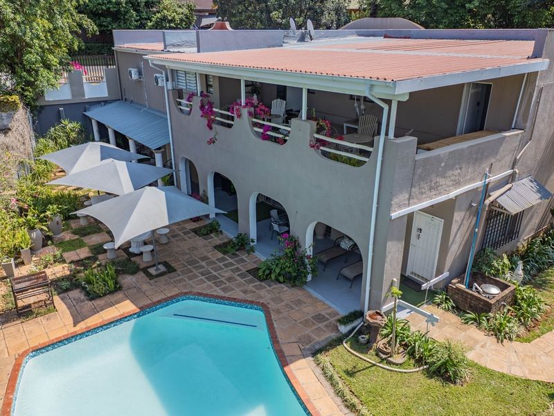 Aerial view of the rear exterior featuring a swimming pool, paved patio area, and a two-story structure with a balcony and covered ground-floor patio.