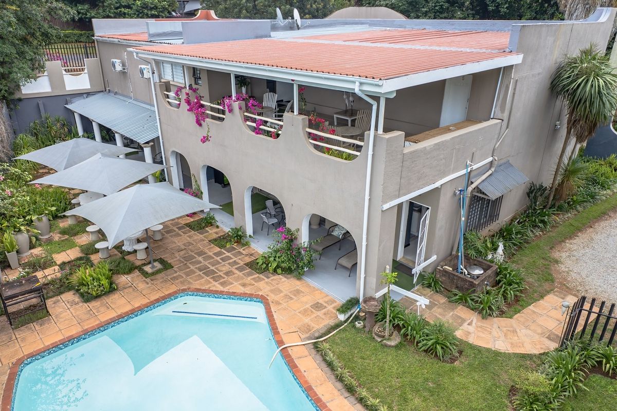 Aerial view of a multi-level property featuring a swimming pool, expansive tiled patio, covered balcony with arched detailing, and established garden areas.