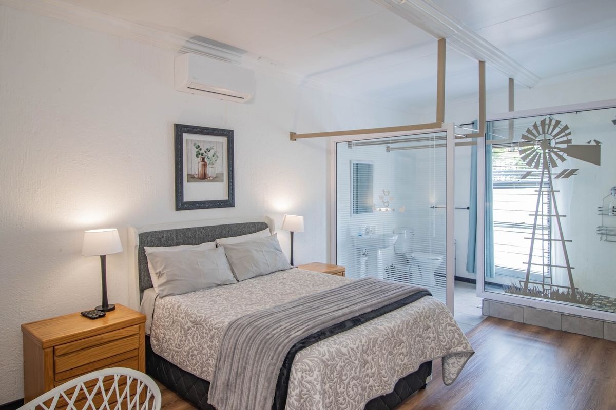 A well-maintained bedroom featuring laminate flooring, crown molding, a wall-mounted air conditioner, and an integrated en-suite bathroom with a glass partition.