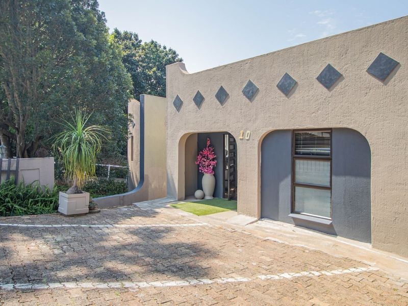 Front elevation of the property featuring a paved driveway, arched entrance, and textured stucco facade with decorative diamond accents.