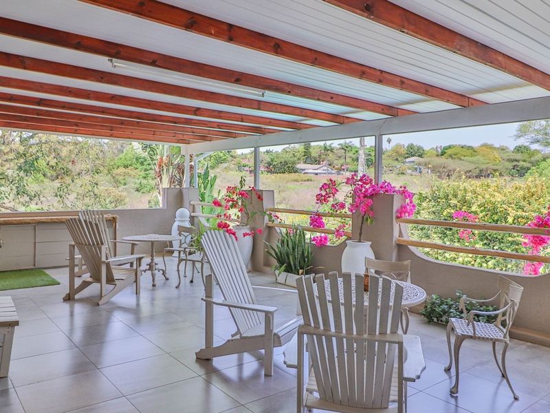 Spacious covered patio featuring tiled flooring, exposed timber beams, and a built-in counter, offering scenic views of the surrounding landscape.