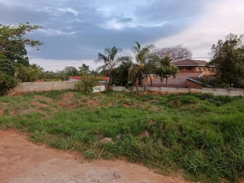 A vacant residential plot featuring a precast boundary wall, electric fencing, and uneven, grass-covered terrain ready for development.