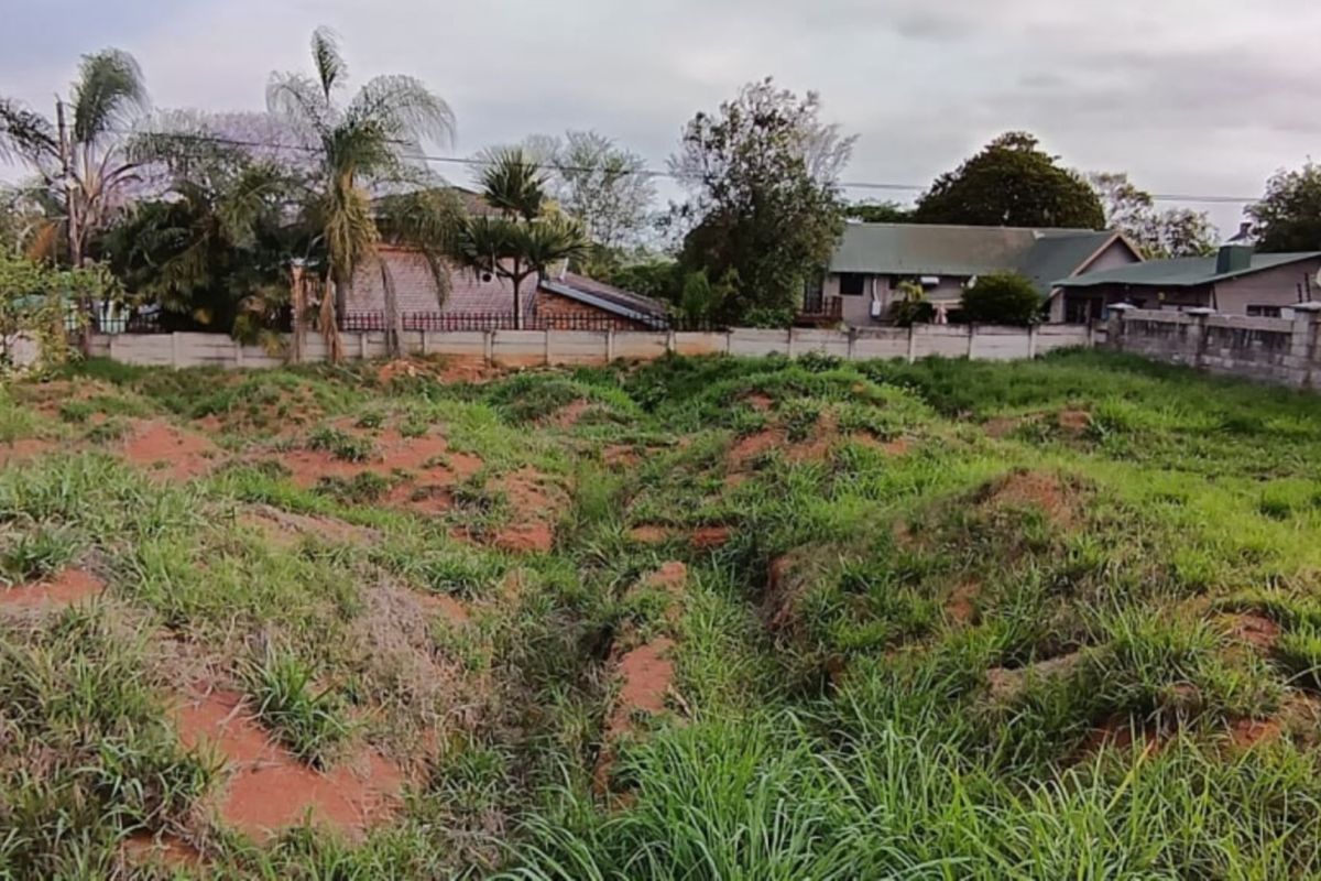 A vacant residential plot featuring uneven terrain and overgrown grass, enclosed by perimeter boundary walls in a suburban neighborhood setting.