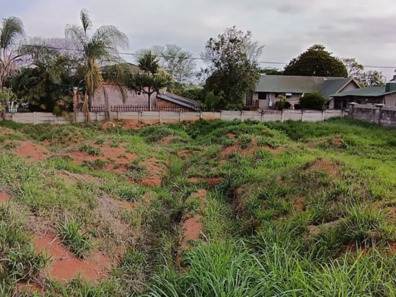 A vacant residential plot featuring uneven terrain and overgrown grass, enclosed by perimeter boundary walls in a suburban neighborhood setting.