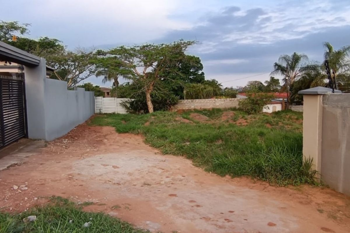 A vacant residential plot featuring a perimeter wall, sliding gate, and security fencing, providing a secure foundation for future development.