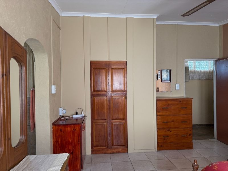 A bedroom featuring tiled flooring, a ceiling fan, and a built-in wooden cupboard, with an arched doorway leading to an adjacent space.