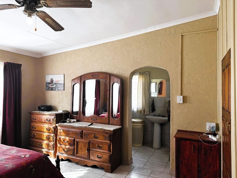 Bedroom featuring a ceiling fan, textured walls, and an arched entryway leading to an en-suite bathroom with a pedestal basin.