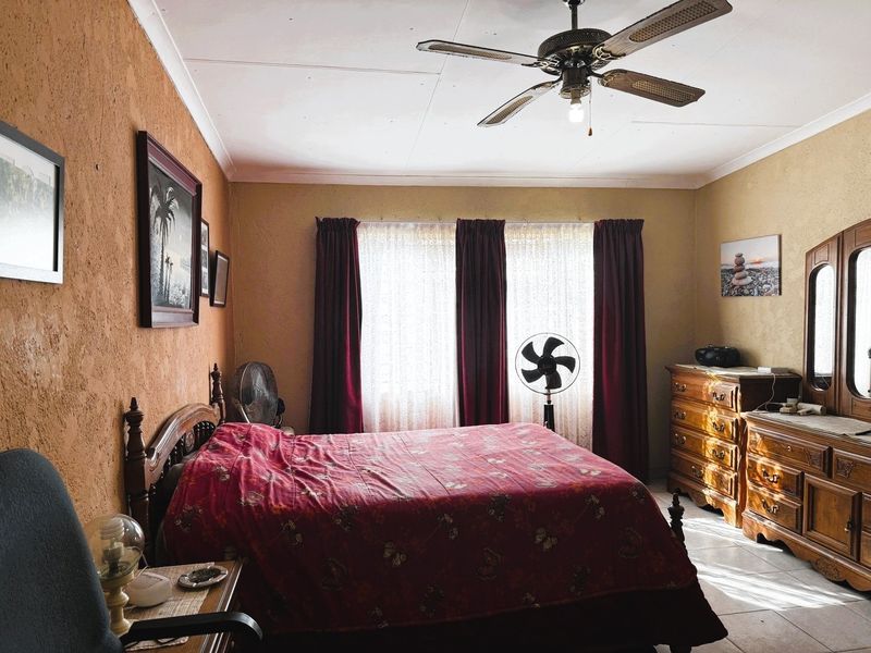 A bedroom featuring tiled flooring, a ceiling fan, and textured walls, offering a dated aesthetic that could benefit from modern updates.