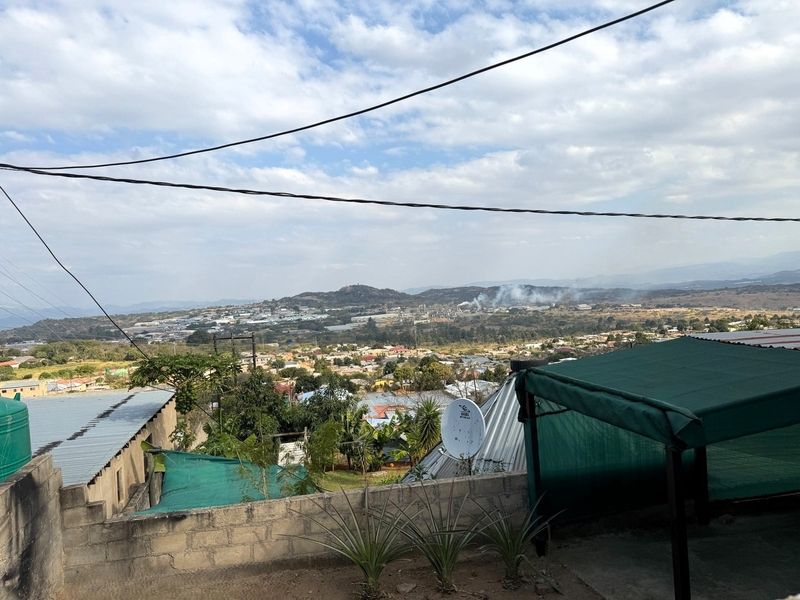 An elevated view overlooking a residential neighbourhood and surrounding landscape, featuring a satellite dish and concrete boundary wall in the foreground.