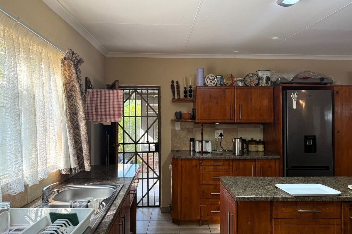 A functional kitchen featuring wooden cabinetry, granite countertops, a central island, and direct access to an outdoor area through a security gate.