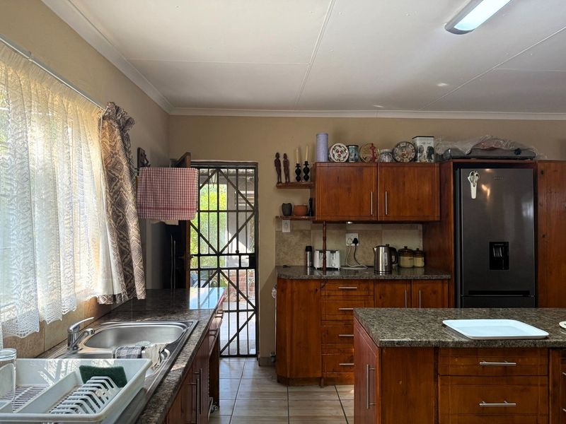 A functional kitchen featuring wooden cabinetry, granite countertops, a central island, and direct access to an outdoor area through a security gate.