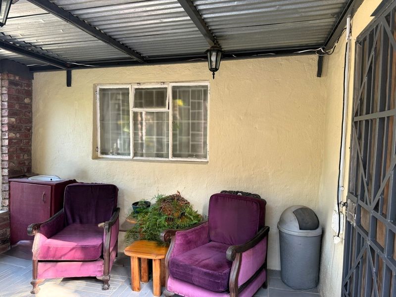 A covered patio area featuring a corrugated metal roof, security window bars, and a brick pillar, providing a functional outdoor space.