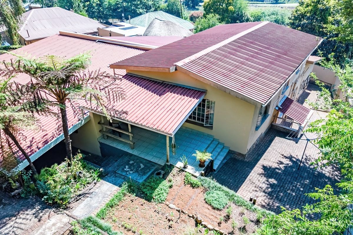 Aerial view of the property showing the main house structure, corrugated metal roofing, covered patio area, and paved outdoor spaces.