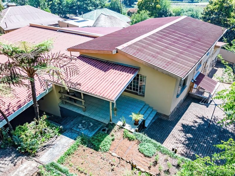 Aerial view of the property showing the main house structure, corrugated metal roofing, covered patio area, and paved outdoor spaces.