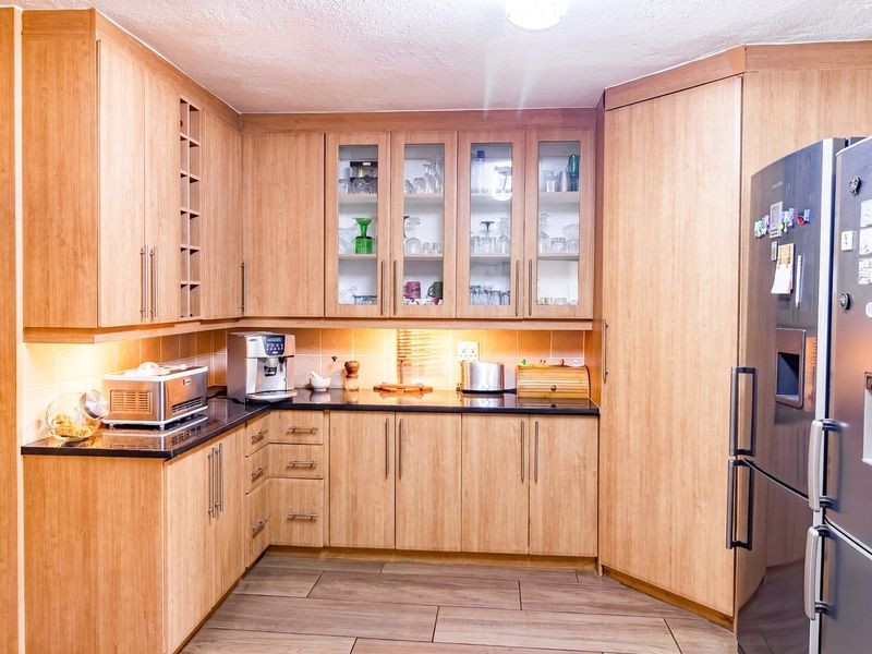 A functional kitchen featuring light wood-look laminate cabinetry, granite countertops, glass-front display units, and integrated storage solutions with under-cabinet lighting.