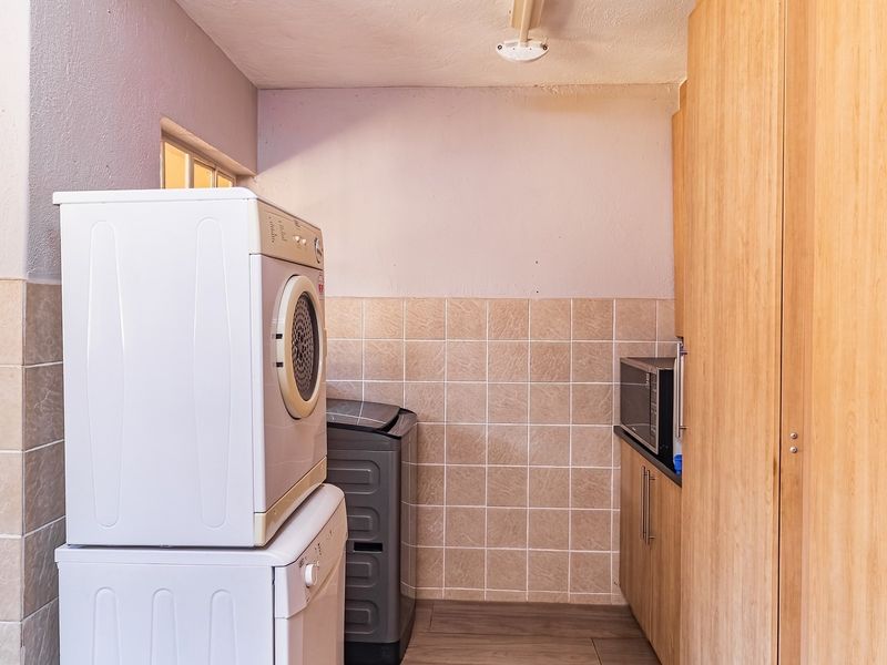 A functional laundry area featuring built-in cabinetry, tiled splashbacks, and dedicated space for laundry appliances.
