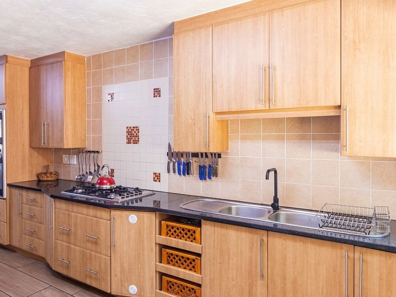 A functional kitchen featuring light wood cabinetry, dark laminate countertops, a gas hob, built-in oven, and a double stainless steel sink with tiled backsplash.
