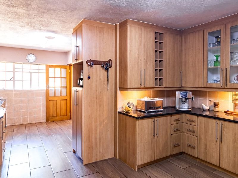 A well-maintained kitchen featuring warm-toned wooden cabinetry, black granite countertops, integrated storage solutions, and tiled flooring with ample natural light.