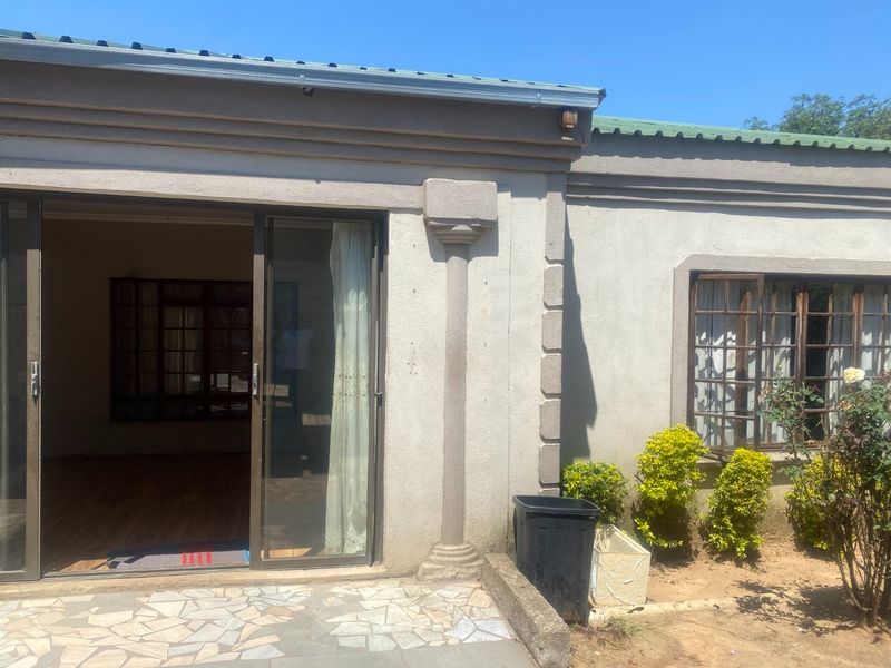 Rear exterior view of the house featuring a stone-paved patio, sliding glass doors, and decorative architectural pillars.