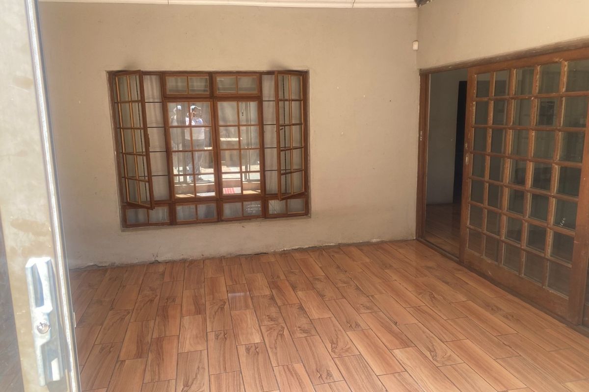 An empty living area featuring wood-look tiled flooring, a wooden-framed casement window, and a sliding door leading to an adjacent room.