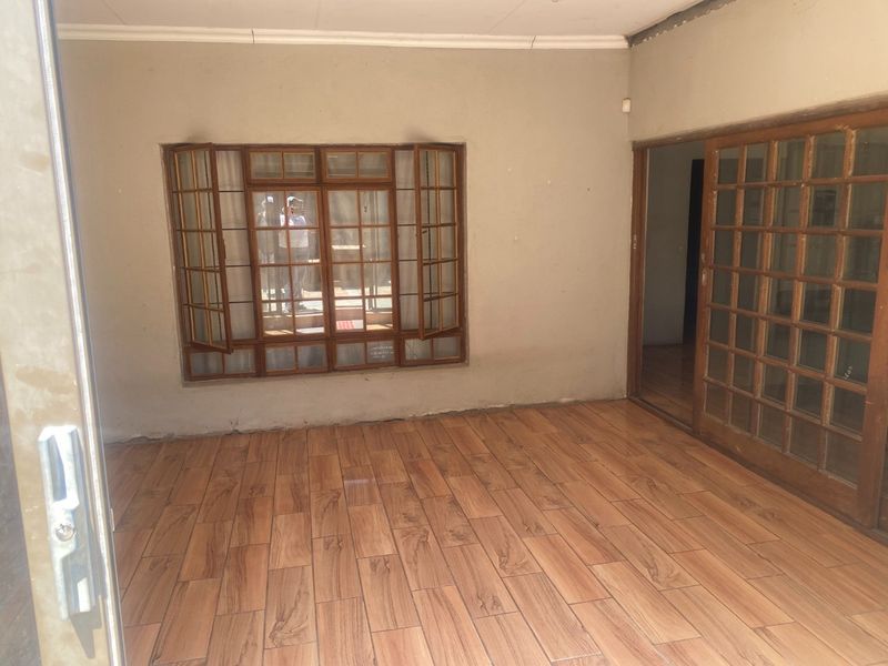 An empty living area featuring wood-look tiled flooring, a wooden-framed casement window, and a sliding door leading to an adjacent room.