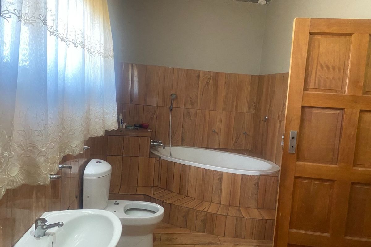 Bathroom featuring a built-in bathtub with wood-look tile surround, pedestal basin, and toilet. The room requires finishing touches to the ceiling and wall plaster.
