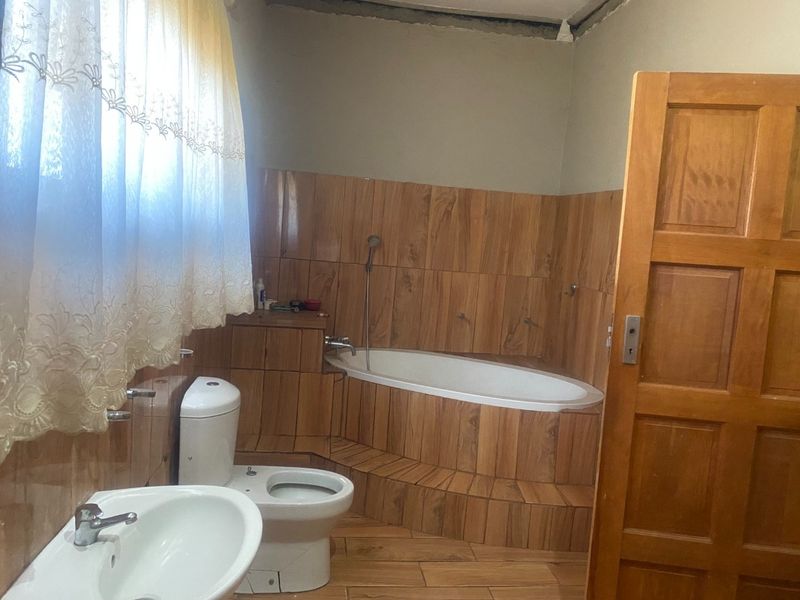 Bathroom featuring a built-in bathtub with wood-look tile surround, pedestal basin, and toilet. The room requires finishing touches to the ceiling and wall plaster.