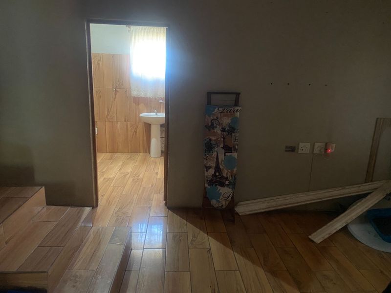 A view from a tiled hallway looking into a bathroom featuring a pedestal basin and wood-look floor tiles, currently in an unfinished state.