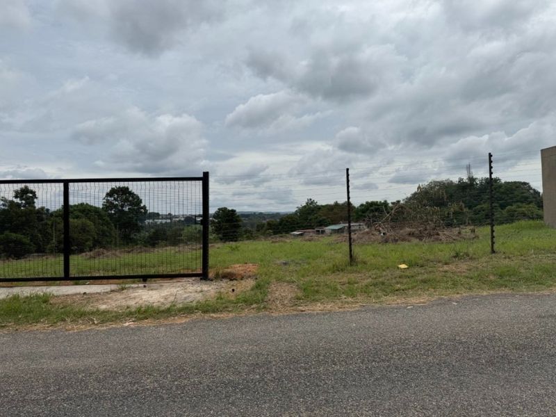 A vacant residential plot featuring street-level access, a metal mesh gate, and perimeter electric fencing, offering a clear view of the surrounding landscape.