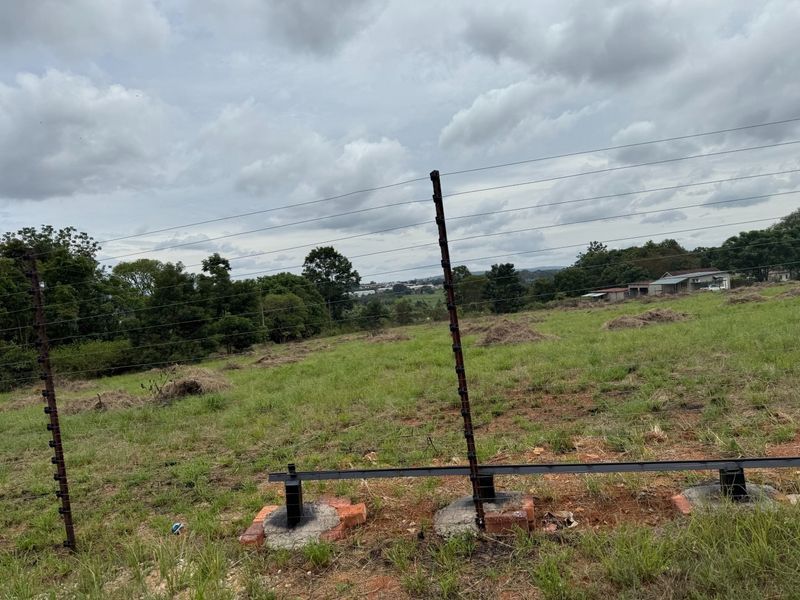 A view of a vacant residential plot featuring installed electric fencing with steel posts and concrete footings.