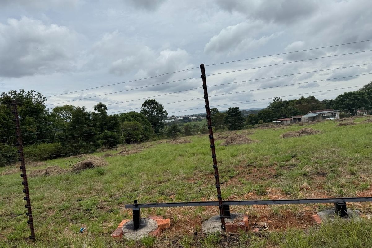 A view of a vacant residential plot featuring installed electric fencing with steel posts and concrete footings.