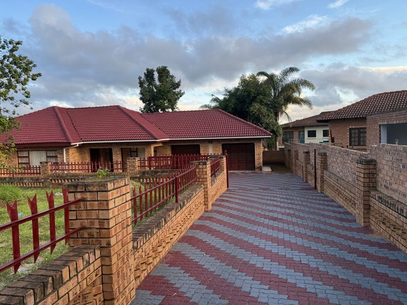 Front view of a facebrick house featuring a paved driveway, double garage, and secure perimeter wall with metal fencing.
