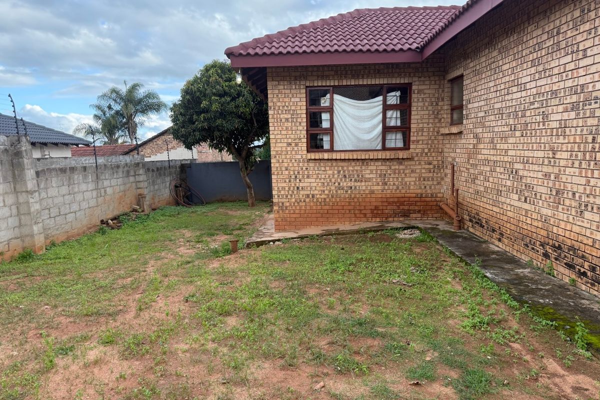 Rear exterior view of a face brick house featuring a tiled roof, concrete boundary wall with electric fencing, and a small garden area.