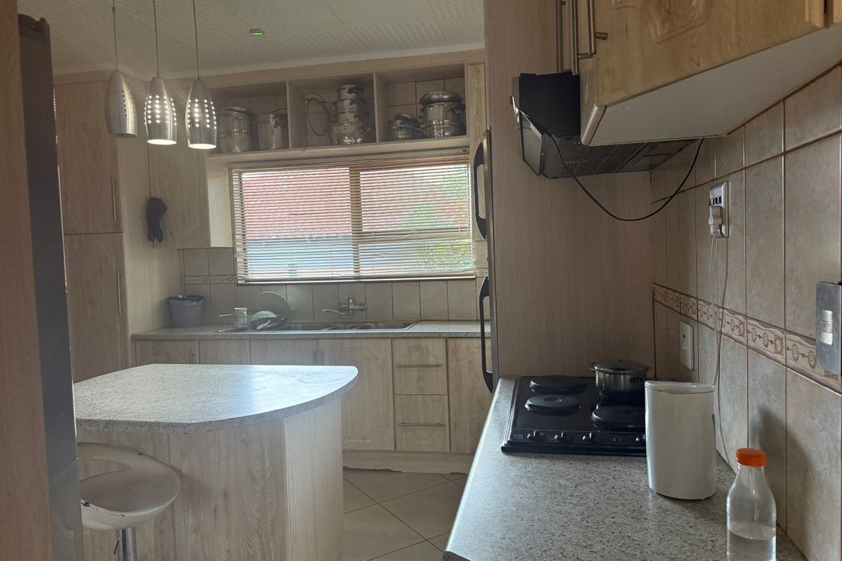 A functional kitchen featuring light wood-look cabinetry, laminate countertops, a central island, and an integrated electric hob with extractor fan.