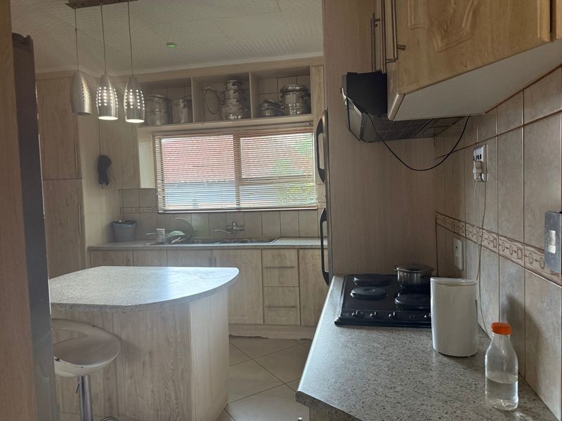 A functional kitchen featuring light wood-look cabinetry, laminate countertops, a central island, and an integrated electric hob with extractor fan.