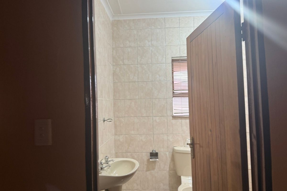 A functional bathroom featuring tiled walls, a pedestal basin, and a standard toilet, viewed through a wooden door frame.