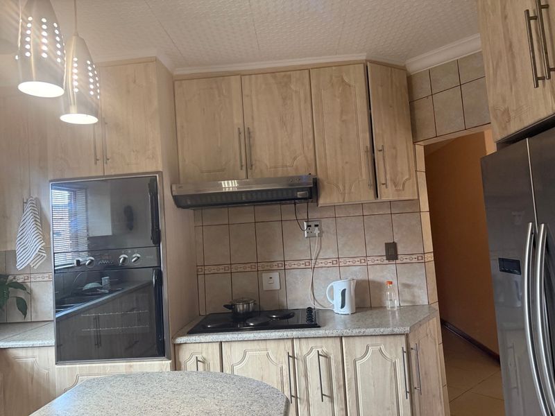 A functional kitchen featuring light wood-finish cabinetry, tiled backsplash, built-in oven, and electric hob with an integrated extractor fan.