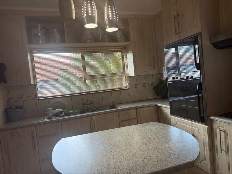 A functional kitchen featuring light wood-finish cabinetry, laminate countertops, a double bowl sink, and a built-in oven with a tiled backsplash.