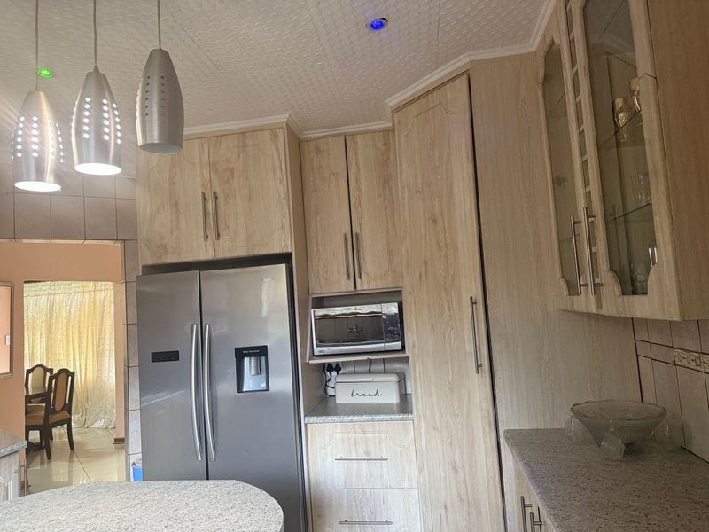 A functional kitchen featuring light wood-look laminate cabinetry, granite countertops, and integrated microwave space, with a view into the adjacent dining area.