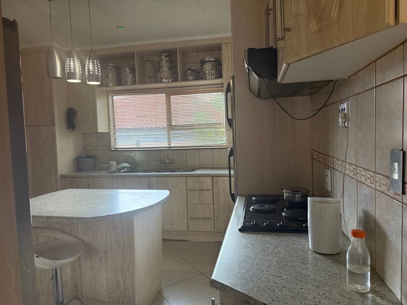 A functional kitchen featuring light wood-look laminate cabinetry, stone-patterned countertops, a built-in electric hob with extractor, and a central island for additional workspace.