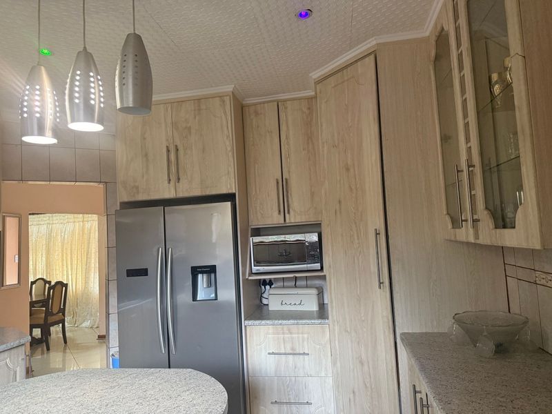 A functional kitchen featuring light wood-grain cabinetry, granite countertops, built-in microwave, and modern pendant lighting, with an open flow to the adjacent dining area.