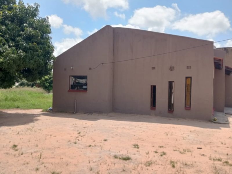 Rear view of a single-story residential house featuring plastered masonry walls and a mix of vertical and square window openings.