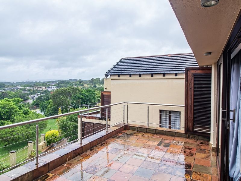 A spacious covered balcony featuring tiled flooring, a stainless steel balustrade, and expansive views of the surrounding landscape.