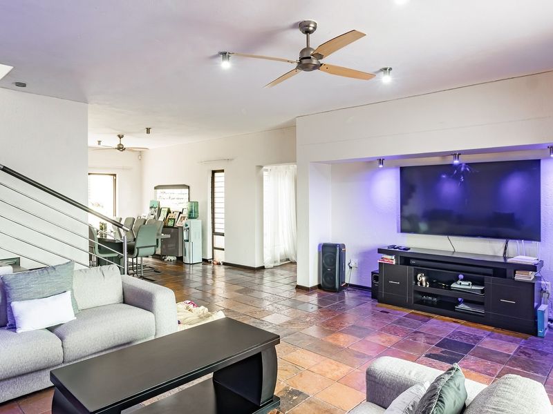 Spacious open-plan living area featuring stone tile flooring, a built-in media alcove, and a modern staircase with metal railings.