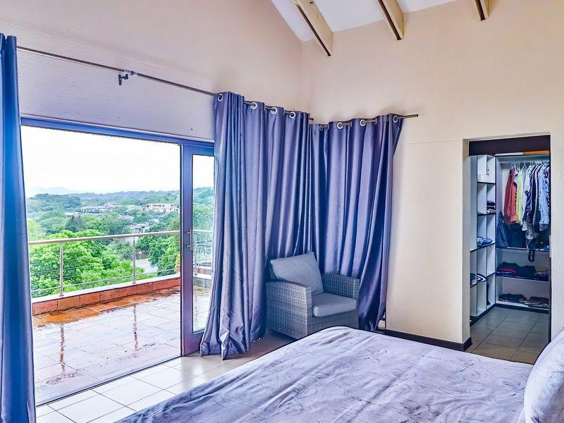 Spacious bedroom featuring a vaulted ceiling with exposed rafters, tiled flooring, and a walk-in closet, with direct access to a private balcony.