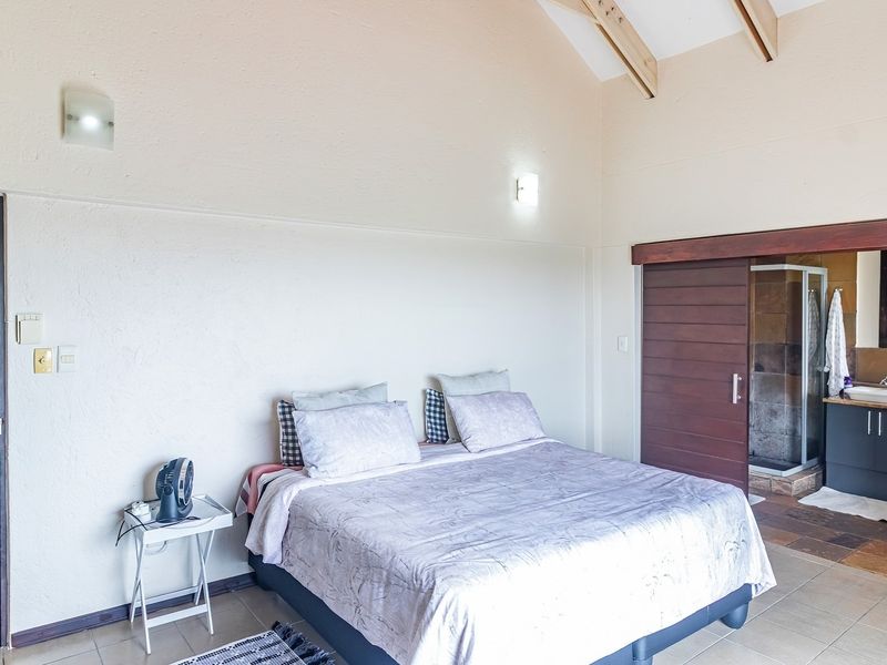 Spacious bedroom featuring a vaulted ceiling with exposed timber rafters, tiled flooring, and a sliding timber door leading to an en-suite bathroom.